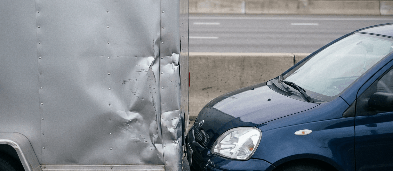 A blue car has collided with the rear of a truck, leaving visible impact damage on both vehicles.