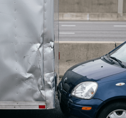A blue car has collided with the rear of a truck, leaving visible impact damage on both vehicles.