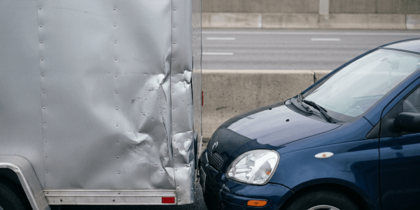A blue car has collided with the rear of a truck, leaving visible impact damage on both vehicles.